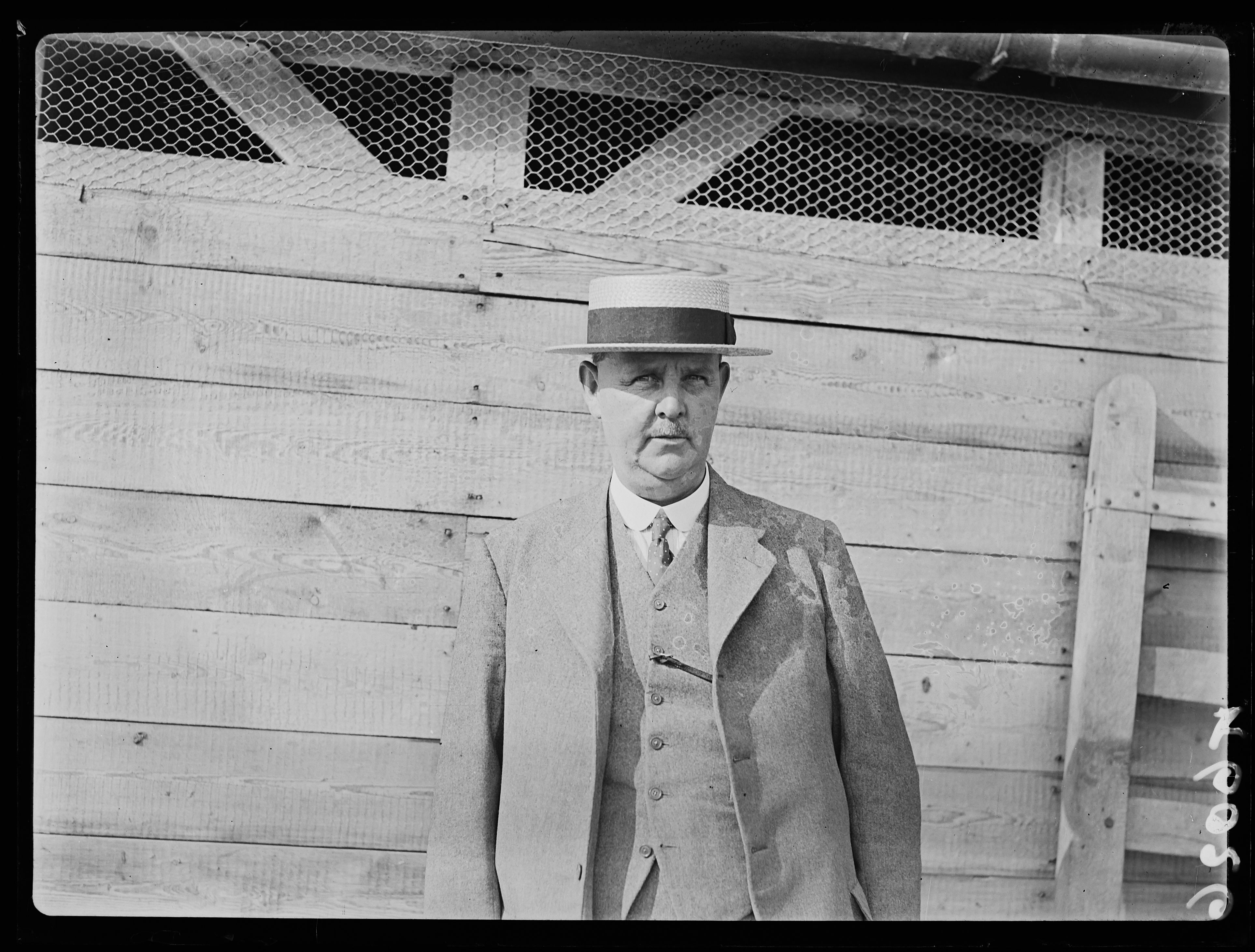 Black and white photograph of a farmer in a suit in front of an animal shed