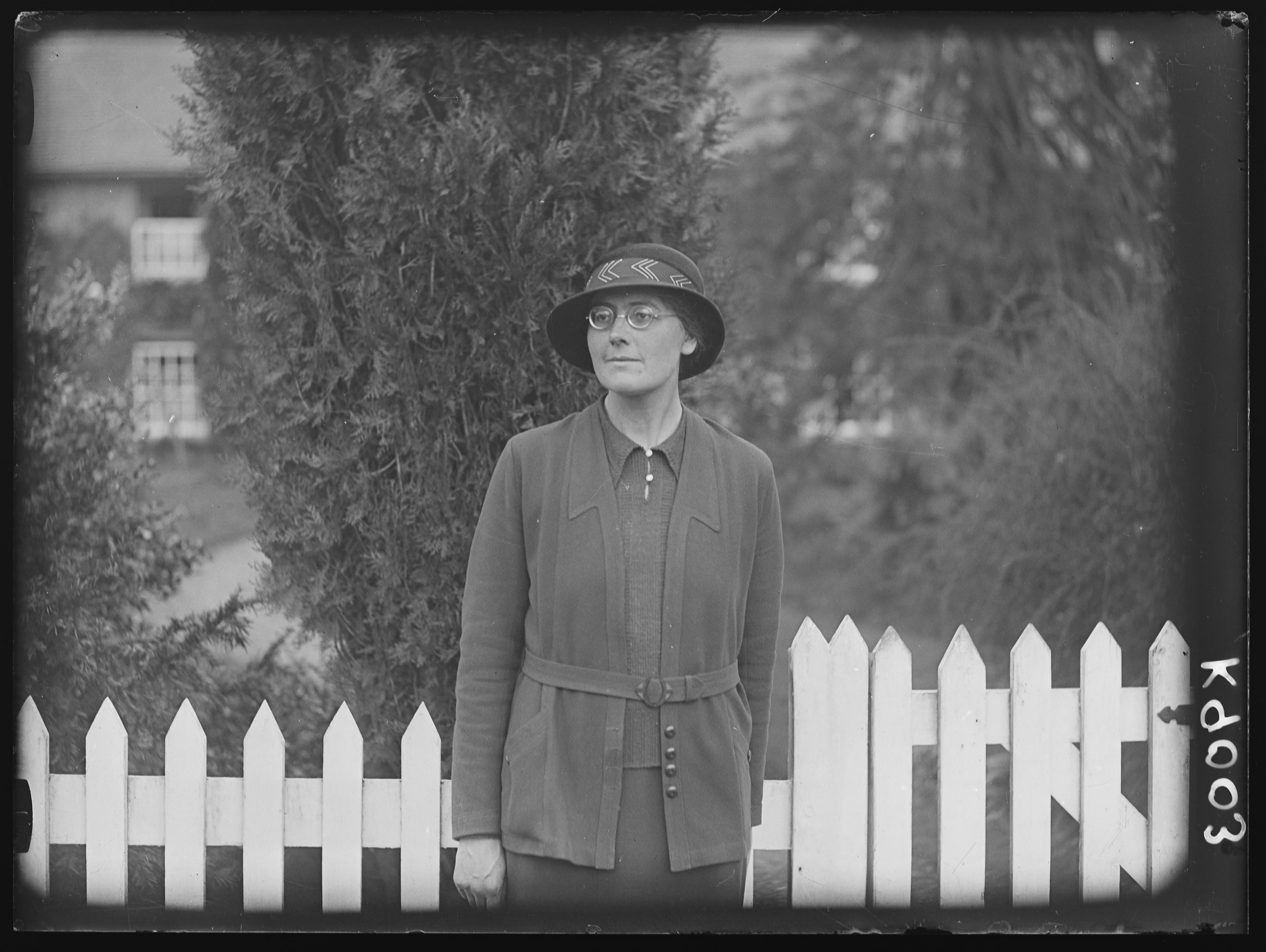 Black and white photograph of a woman in front of a white picket fence