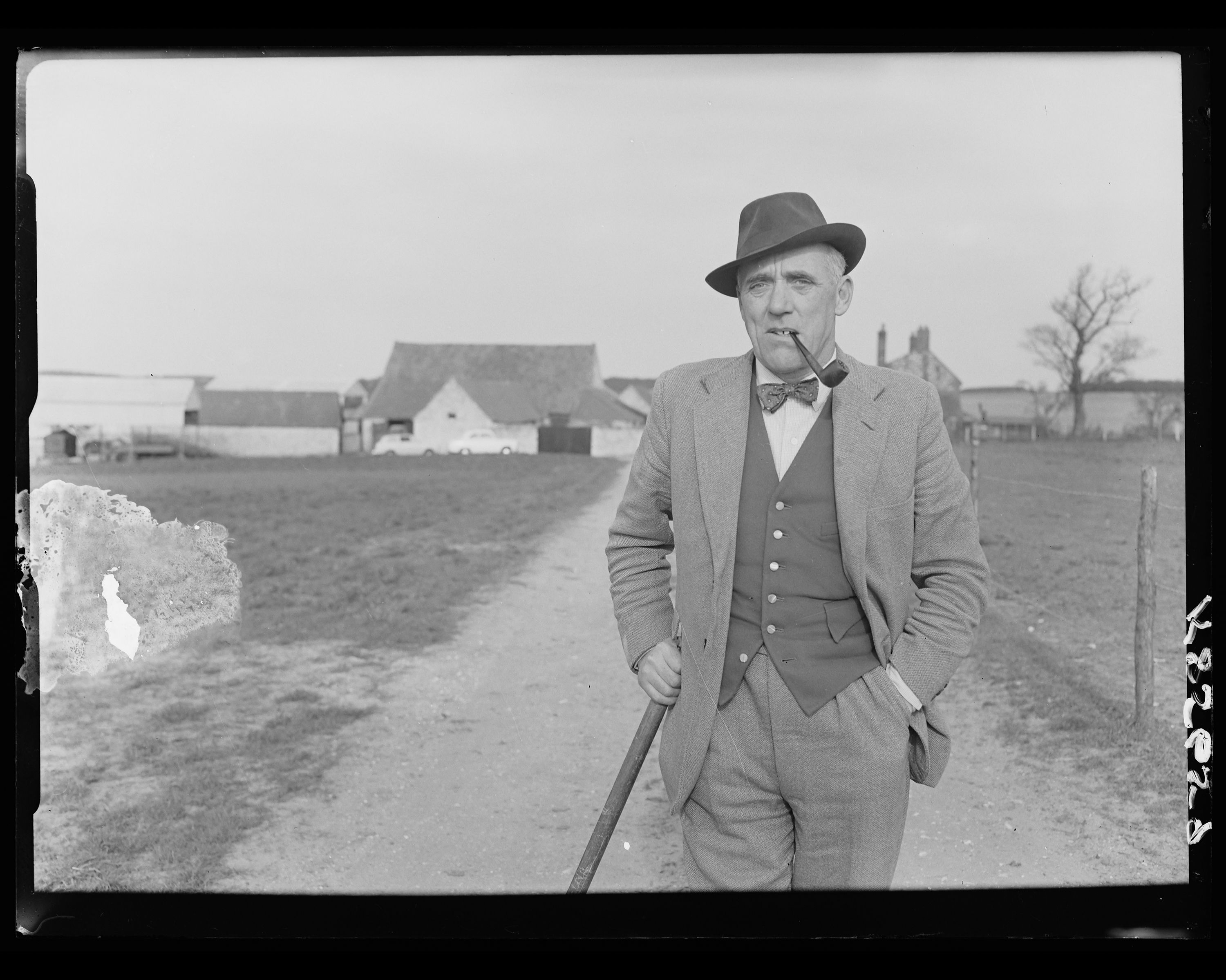 Black and white photograph of a farmer leaning against a stable door with a bull behind him