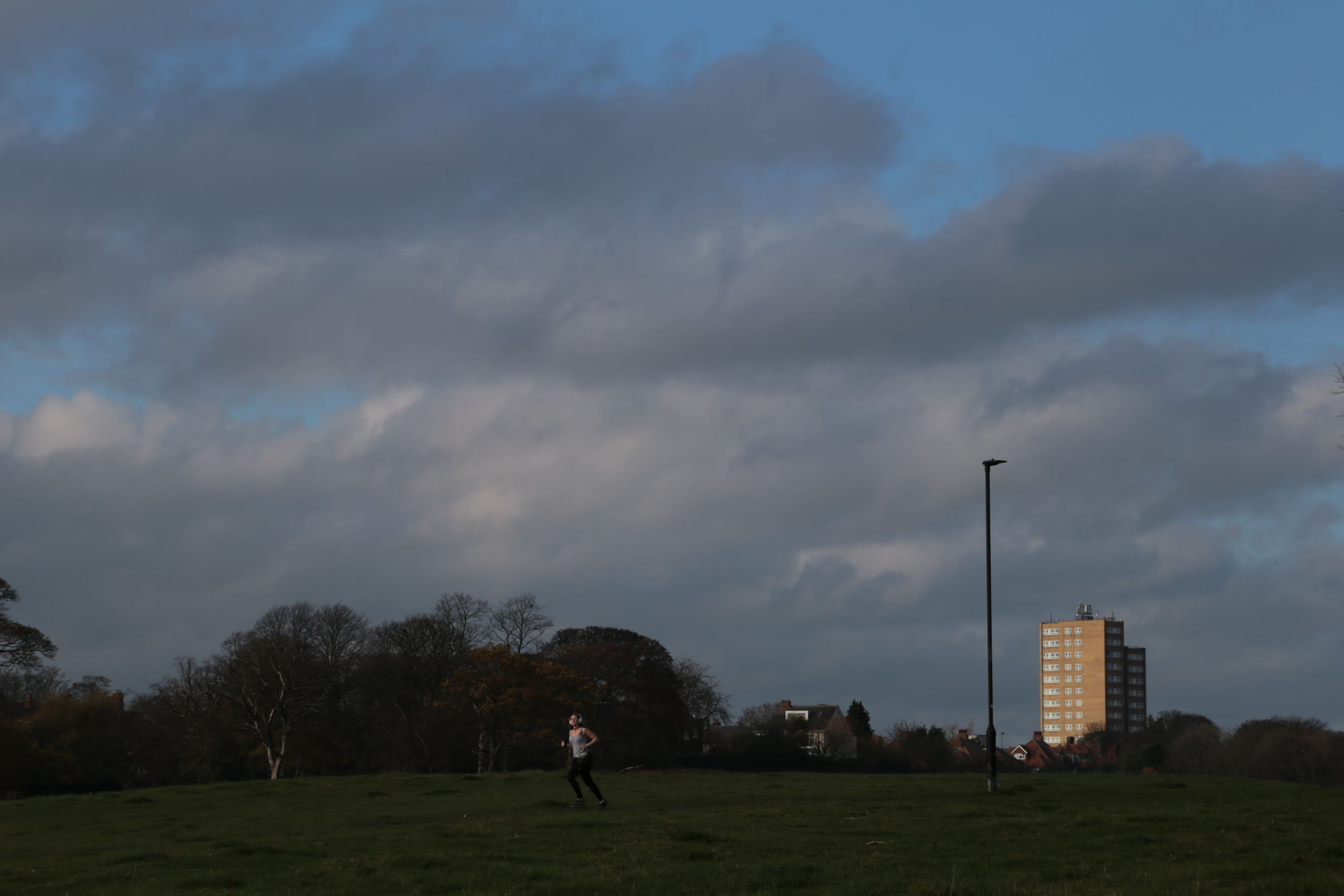 Town moor daylight, clouds, tower block in late sunshine, runner with headphones on